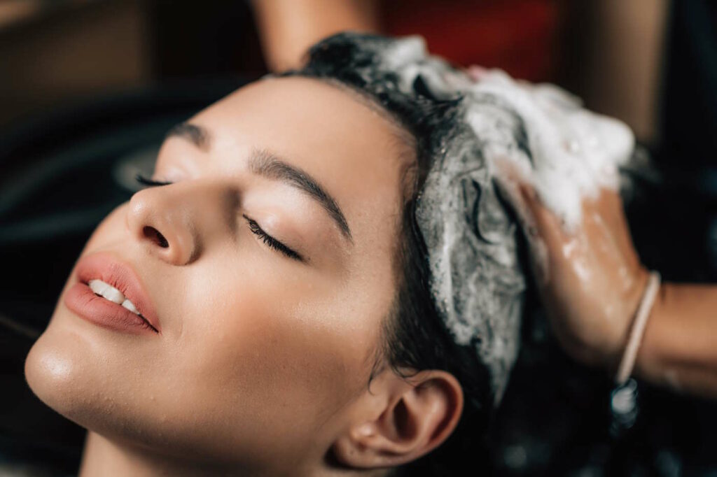 Hairdresser applying shampoo on woman’s hair in beauty salon.